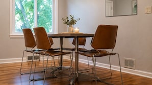 Un coin repas comprenant une table et quatre chaises, un vase avec des fleurs et une fenêtre avec des stores.