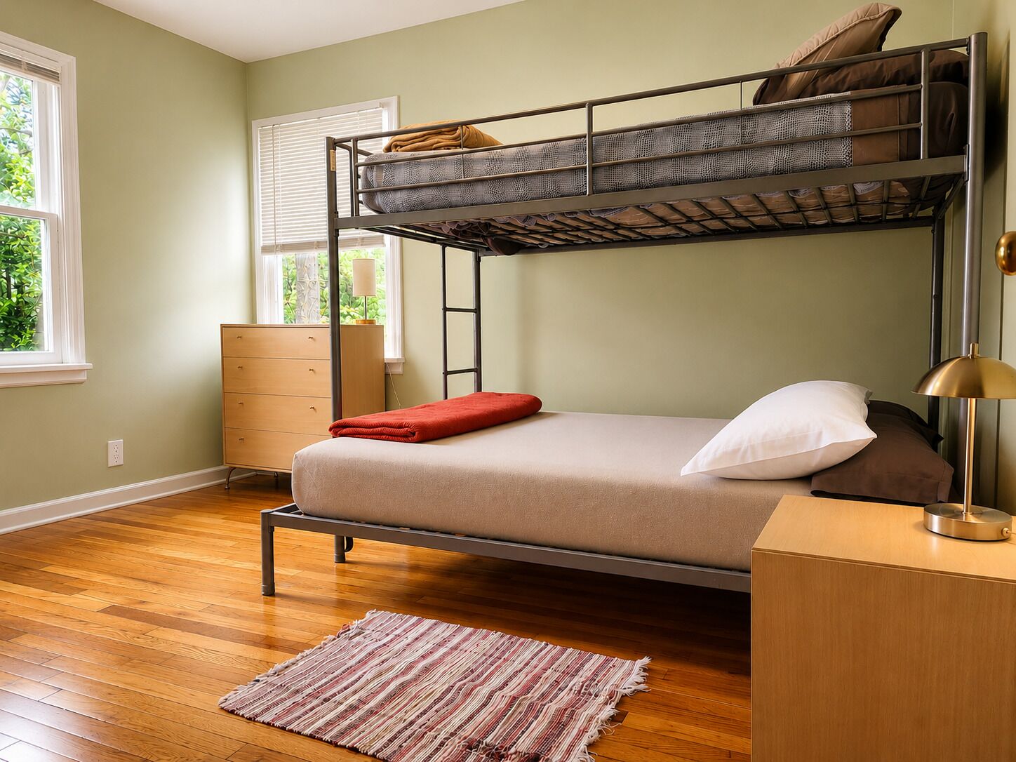 Una cama individual superpuesta con escritorio y lámpara, un aparador y una ventana con persianas.