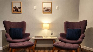 Une pièce avec deux fauteuils violets, une petite table avec une lampe et deux tableaux encadrés accrochés au mur.
