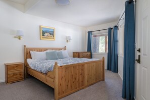 A bedroom with a wooden bed, two bedside tables, a nightstand, a window with curtains, and wall-mounted lamps.
