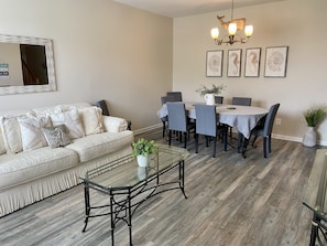 A living room with a sofa, coffee table, dining table with chairs, and a chandelier.