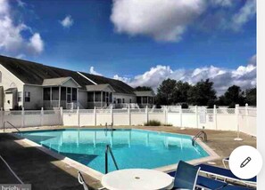 A swimming pool with lounge chairs and a covered area with windows.