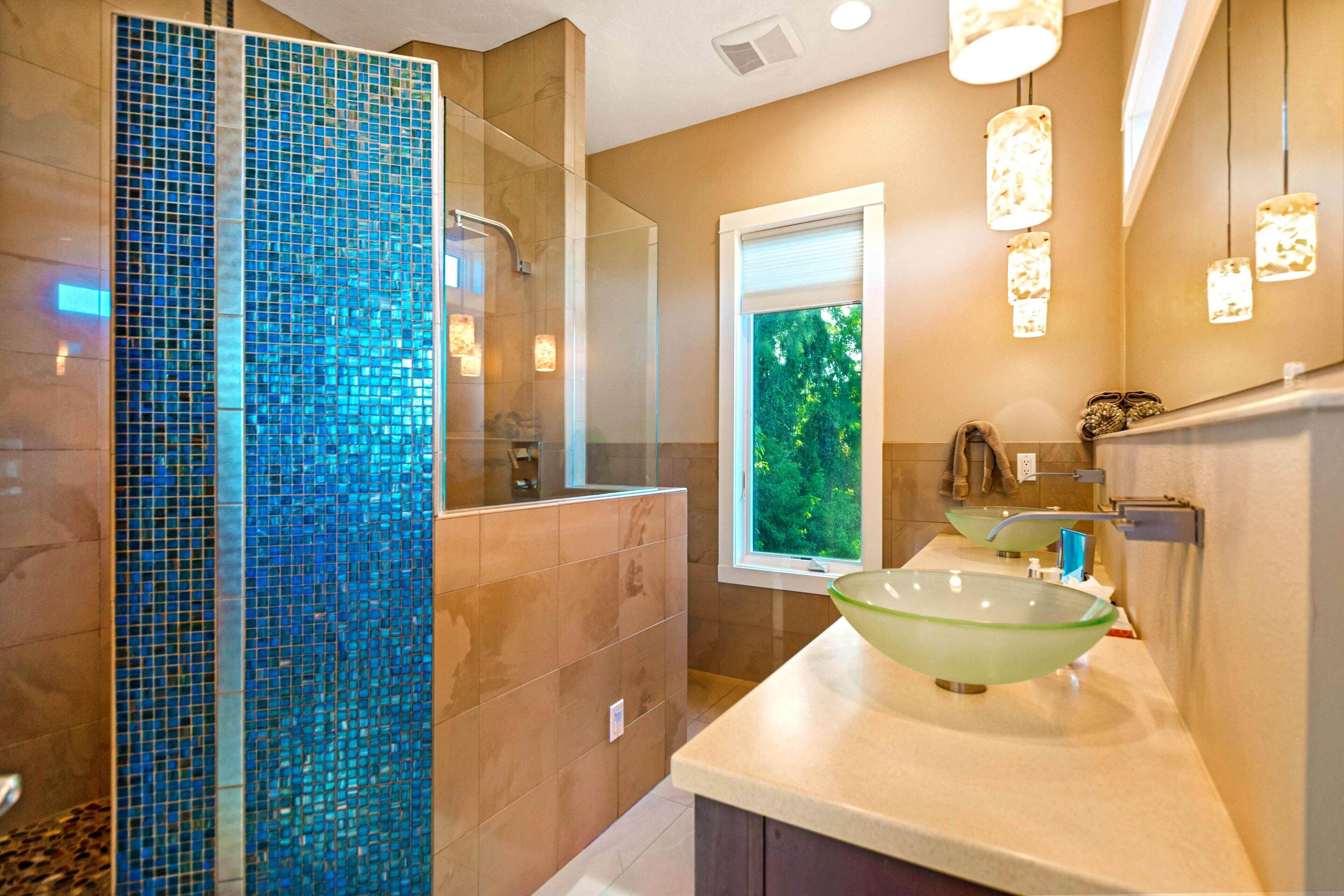 Une salle de bain moderne avec un mur en mosaïque, un grand lavabo en forme de bol en verre et une fenêtre donnant sur un paysage verdoyant.