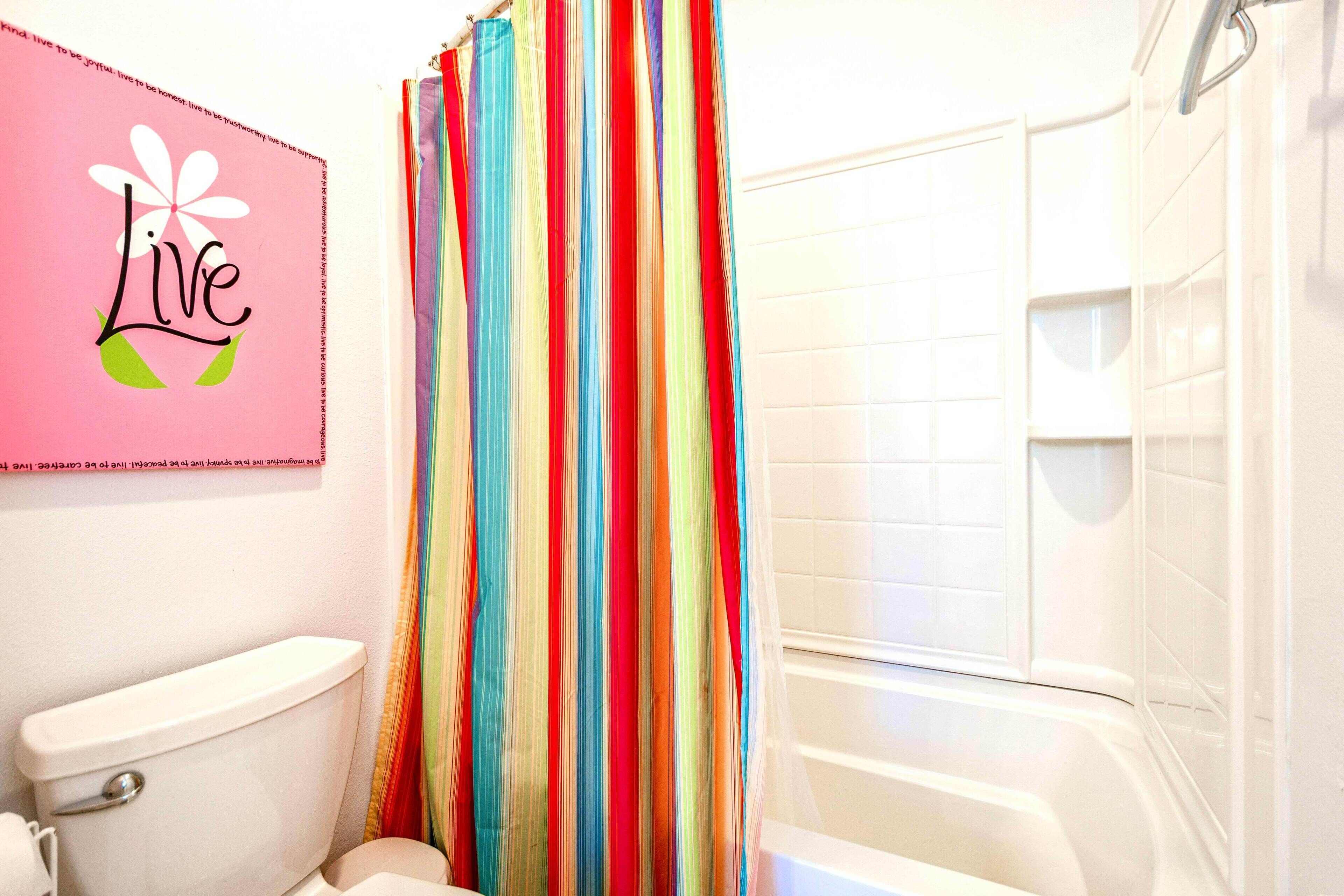 A bathroom with a white toilet, a shower curtain with vertical stripes, and a "Live" sign on the wall.