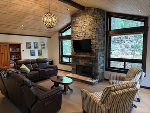 A living room with a stone fireplace, leather furniture, and large windows.