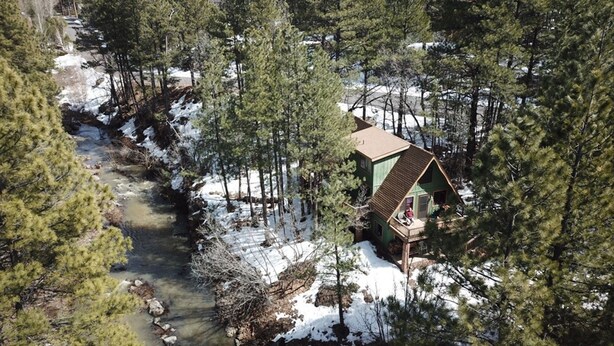 Eine Hütte mit geneigtem Dach, umgeben von dichtem Wald und einem Bach.