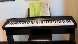 Ein Klavier mit Notenblättern und einem Buch mit dem Titel 'Song BooK' auf einem Notenständer, vor einer Wand mit gerahmten Postern.