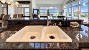 A kitchen with a large island, a double sink, and a view of the ocean.