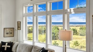 A room with large windows offering a view of the ocean and a grassy landscape. There is a sofa with cushions and a lamp.