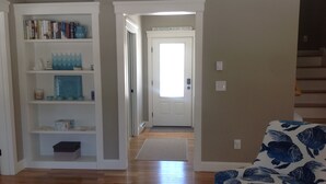 Un corridoio con una porta bianca con su scritto 'CAPE POISE', una libreria e un divano con motivi decorativi.
