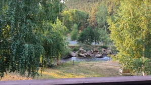 A view from a wooden deck overlooking a river, surrounded by dense green foliage and a prominent rock formation in the distance.