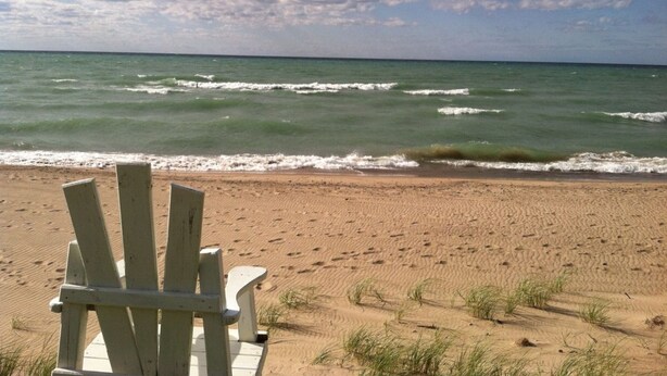 A beach with a wooden chair and a wooden bench facing the ocean.