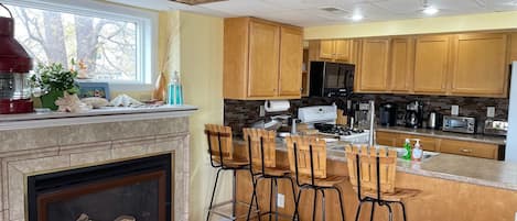 Una cocina moderna con armarios de madera, una isla integrada con taburetes de bar, una chimenea y un ventanal grande.