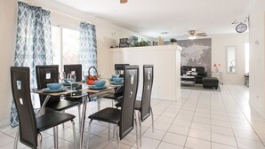 Un coin repas avec une table dressée pour six personnes, des chaises noires et un ventilateur de plafond.