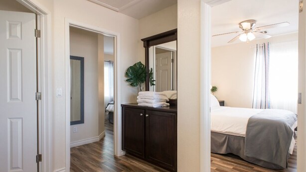 Une chambre à coucher avec un lit, une commode en bois foncé, un miroir et un ventilateur de plafond.