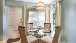 A dining area with a round glass table, wicker chairs, and a hanging light fixture.