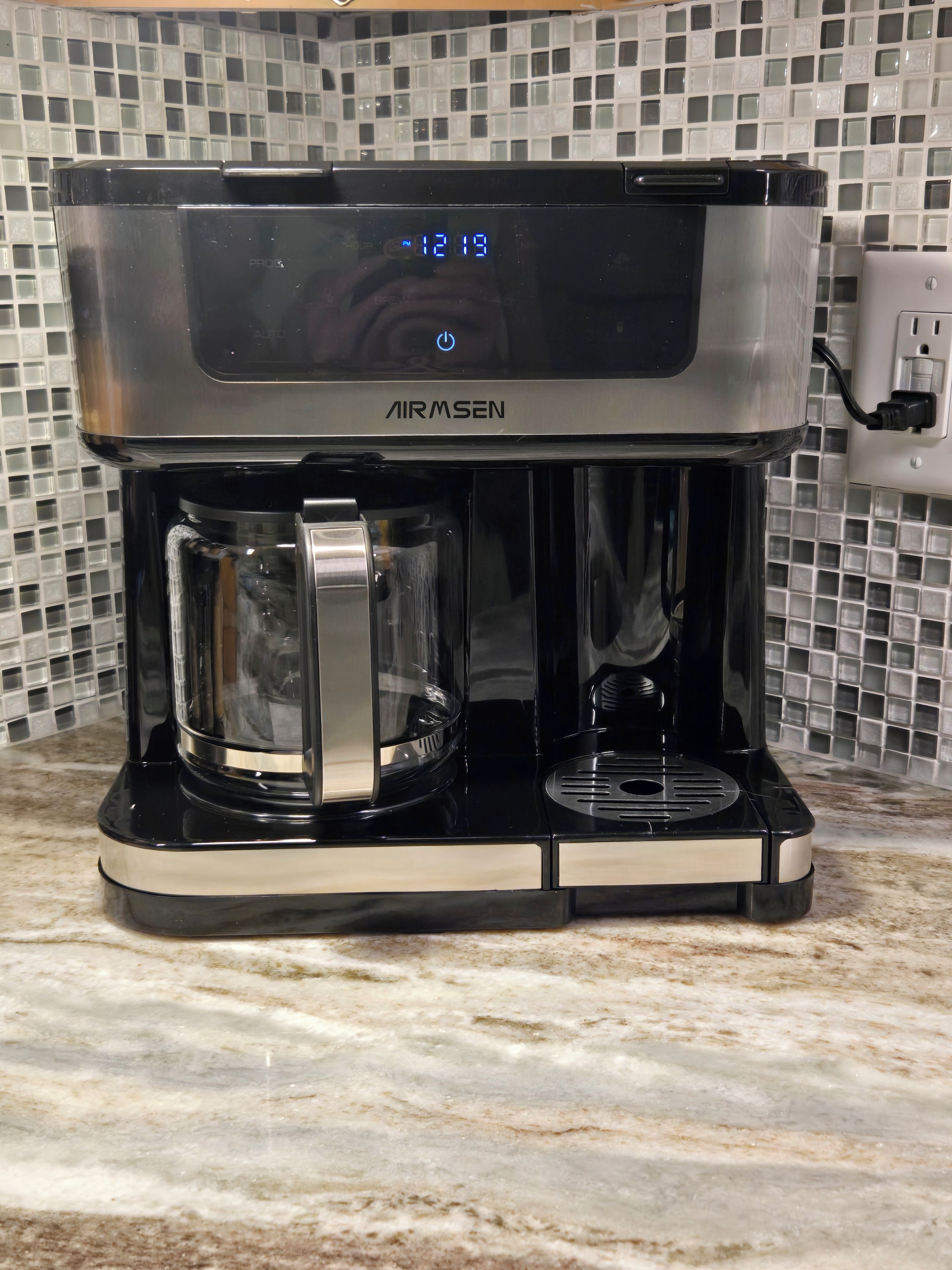 Une machine à café dotée d’un écran numérique, d’une verseuse en verre et d’un réservoir à eau, posée sur un plan de travail.