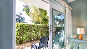 A room with a sliding glass door leading to a garden, a chair, and a small table with a lamp.