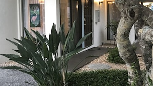 A house with a large glass door, a small garden with plants, and a tree with a hole in the trunk.