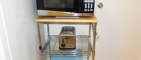A kitchen area with a microwave on a shelf, a toaster, and a box of wine glasses.