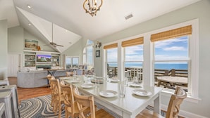 A spacious dining area with a view of the ocean, a kitchen with a lofted ceiling, and a cozy seating area.