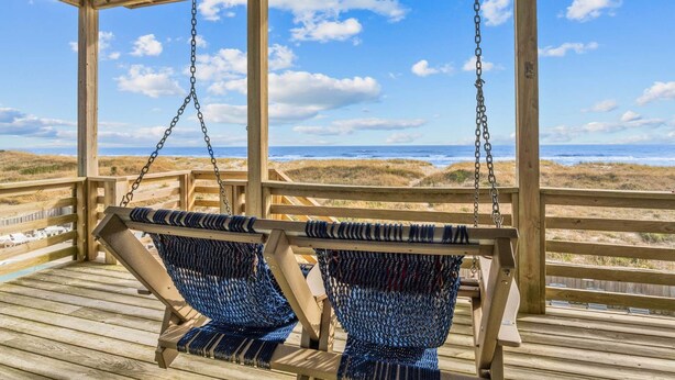A wooden deck with two swing seats overlooking a beach.