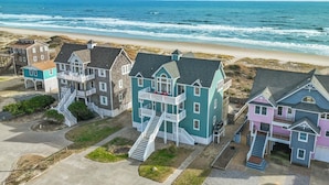 A coastal residential area with houses featuring multiple stories and balconies, adjacent to a beach with visible waves.