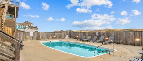 Un jardin avec une piscine, une terrasse en bois et des chaises longues.