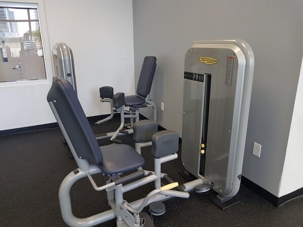 A gym with exercise machines, a window with a view of buildings, and a door.