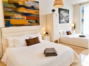 Habitación de hotel con dos camas, un cuadro abstracto grande, un armario y una ventana con vistas.