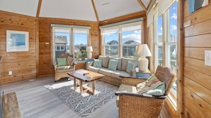 A cozy room with wooden walls, a large window, a sofa, a chair, a table, and a lamp.