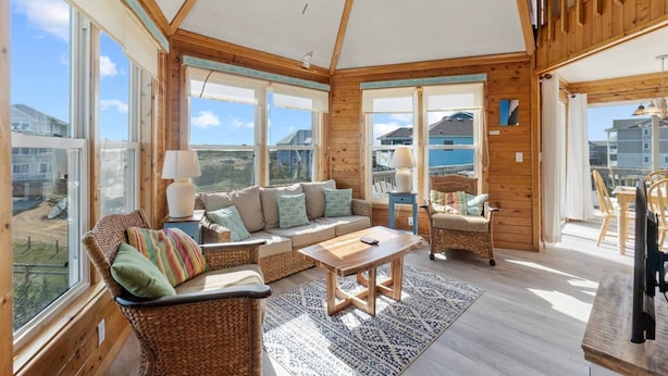 A spacious room with a high ceiling, large windows, a wooden interior, a sofa set, a coffee table, and a view of the outside.