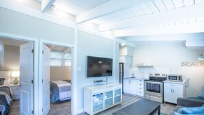 A modern living room with a sofa, coffee table, TV, and kitchenette.