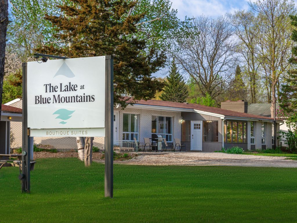 Señalización de 'The Lake at Blue Mountains Boutique Suites' con vista a un edificio que tiene un porche cubierto y un césped al frente.
