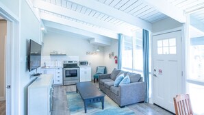 A compact living space with a kitchenette, a gray sofa, a coffee table, and a view through a large window.