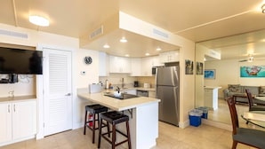 A modern kitchen with white cabinets, a stainless steel refrigerator, and a large island with stools.
