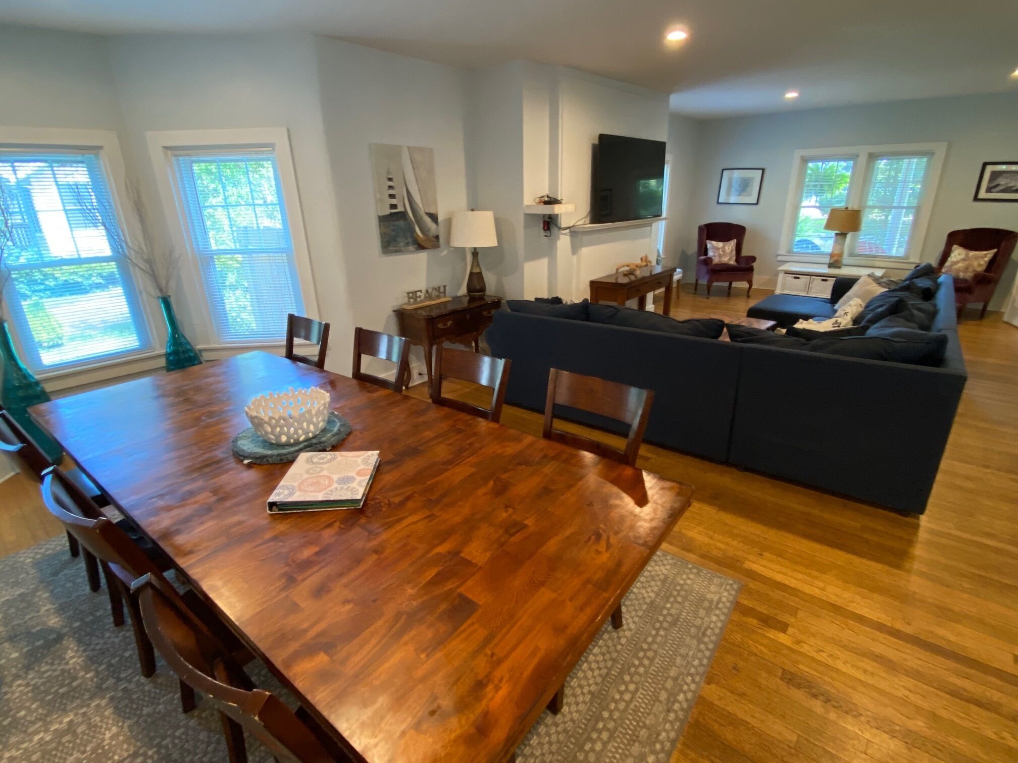 A spacious living room with a wooden dining table, blue sofa, and a flat-screen TV mounted on the wall.