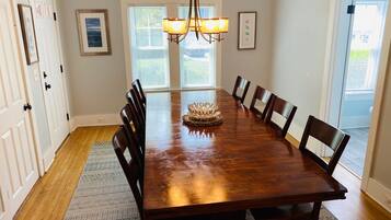 A dining room with a wooden table, eight chairs, a chandelier, and two windows with blinds.