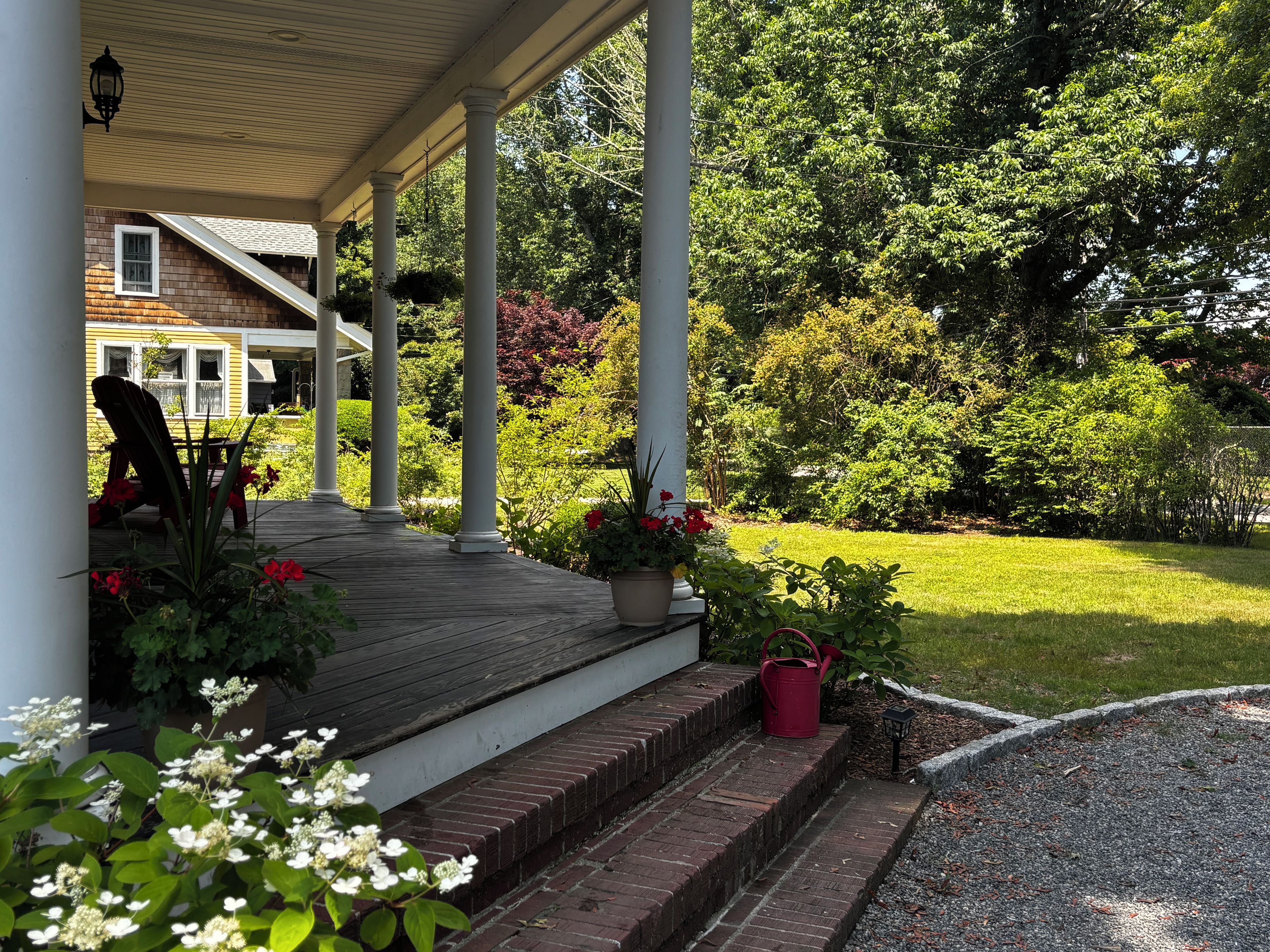 Eine überdachte Veranda mit Treppen zu einem Haus, umgeben von Grünpflanzen und einem Rasen.