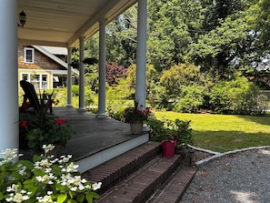 A covered porch with steps leading to a house, surrounded by greenery and a lawn. - Large Historic/updated, Downtown Wakefield - Narragansett Beaches-3 mi. Big yard (South Kingstown)