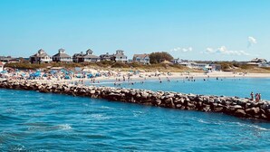 A beach with houses in the background and a rocky breakwater in the foreground.