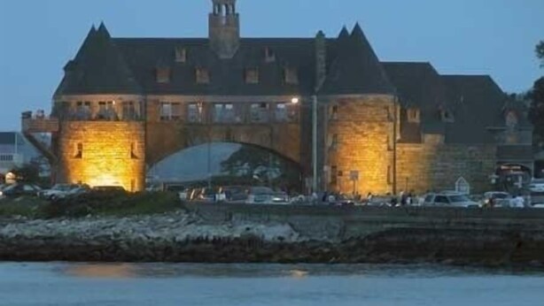 A historic building with a prominent tower and a large archway, situated by a waterfront.
