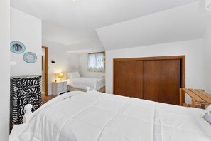 Een slaapkamer met een groot bed, een houten garderobe, een nachtkastje met een lamp en een bijzettafeltje met een zebraprint.