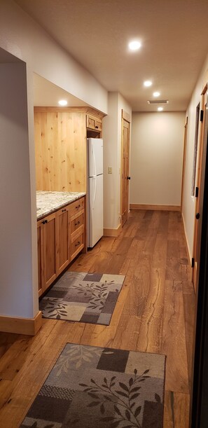 Ein schmaler Flur mit Holzboden, ein Küchenbereich mit Holzausbau und einem Kühlschrank sowie eine Tür zu einem weiteren Raum.