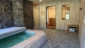 Un área de spa con pared de piedra, una bañera de hidromasaje y suelo de madera.