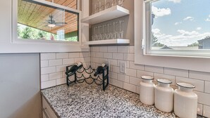 Eine Küche mit weißen Fliesenwänden, einer Arbeitsplatte aus Granit und einem Fenster mit Blick auf Himmel und Bäume.