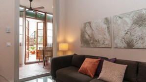 Sala de estar com um sofá marrom escuro, duas almofadas, uma mesa de centro de vidro e uma luminária. Há duas pinturas abstratas na parede e um ventilador de teto.