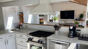 Una cucina moderna con mobili bianchi, piano cottura Bosch, forno integrato, lavastoviglie e macchina per il caffè.