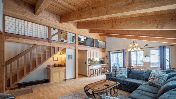 Un amplio salón con una escalera de madera, una cocina y un sofá grande.