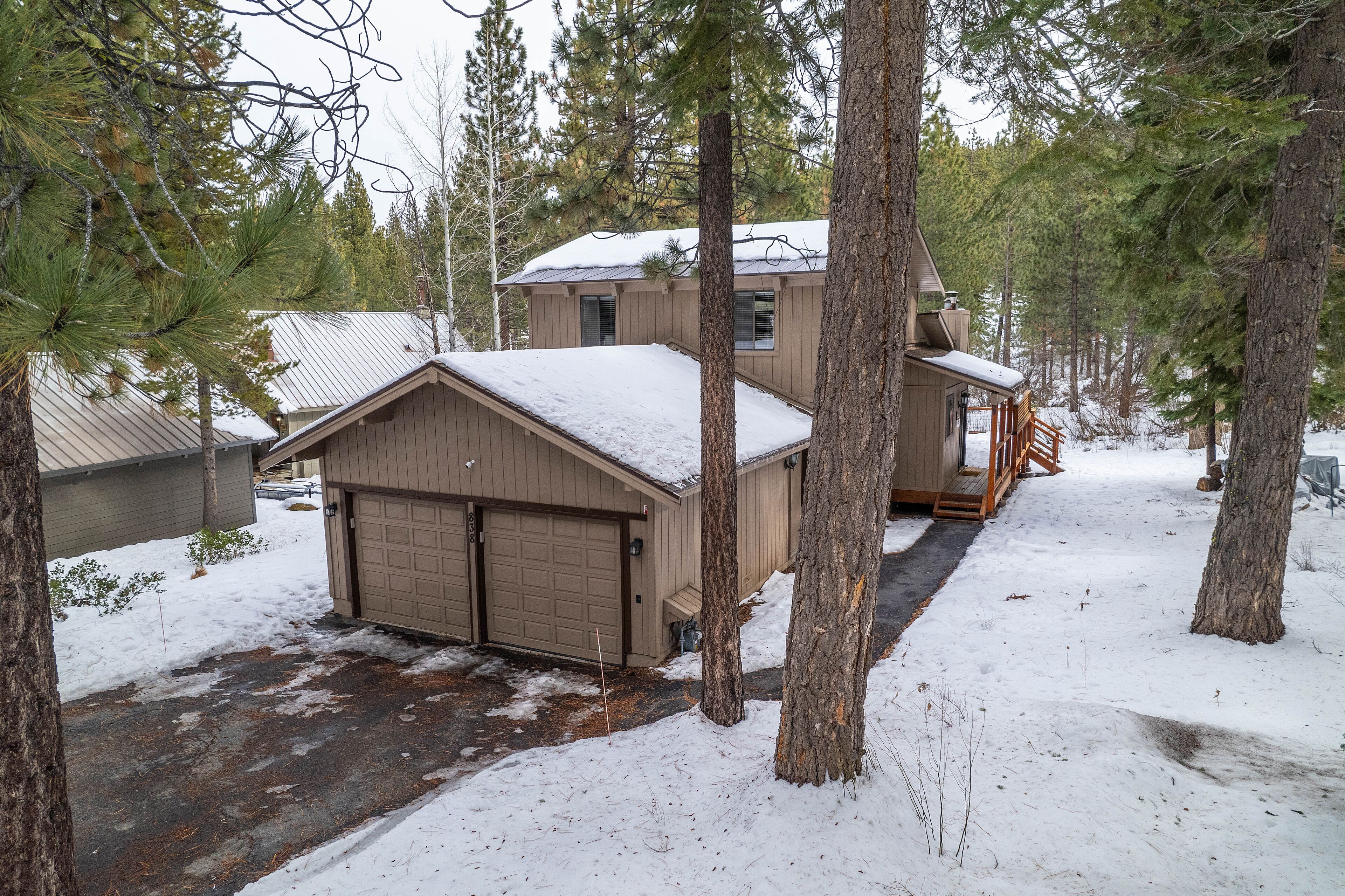 A two-story house with a garage, surrounded by tall pine trees and covered in snow.